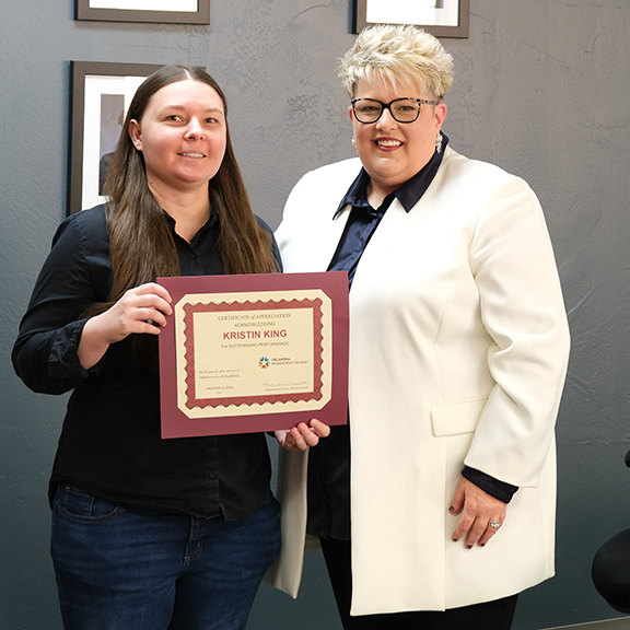 Two women smiling with one holding a certificate.
