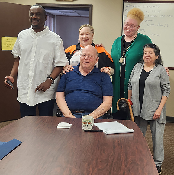 Four people standing behind man who is seated.