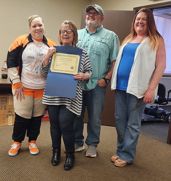 Three people standing behind woman with a certificate.