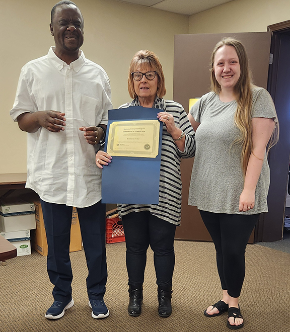 Two people standing alongside woman holding a certificate.