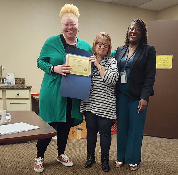 Three women with two holding a certificate.