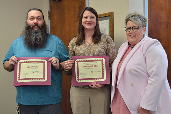 Two people holding awards with third person looking on.