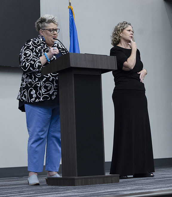 Woman talking on stage using a microphone while a second woman interprets using American Sign Language.