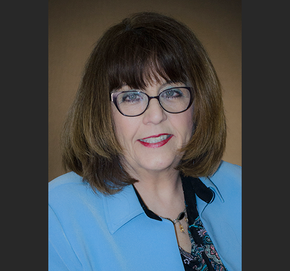 Woman in blue jacket and wearing glasses.