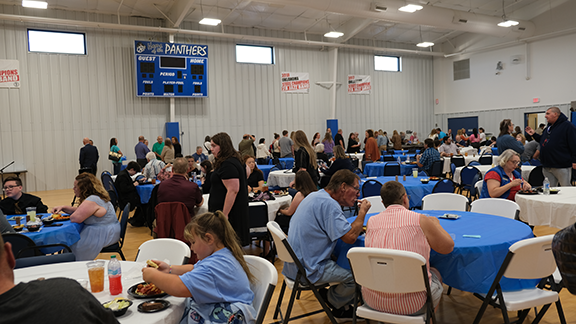 People walking and sitting at tables in a gym.