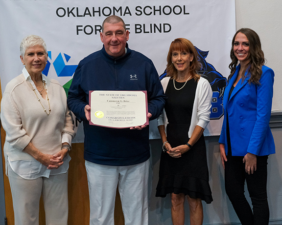 Three women standing next to man with certificate. 