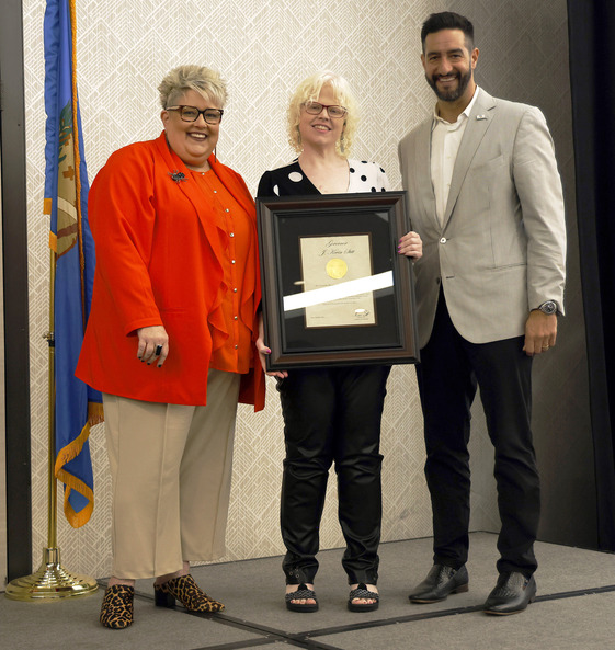 Three people with one woman in the middle holding an award.