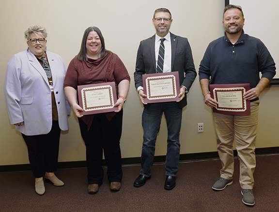 Four people with three holding certificates.