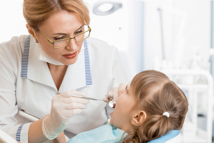 Female dentist leans in to exam young patient's teeth