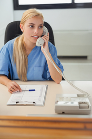 Dental clinic receptionist talks holds phone to her ear at desk