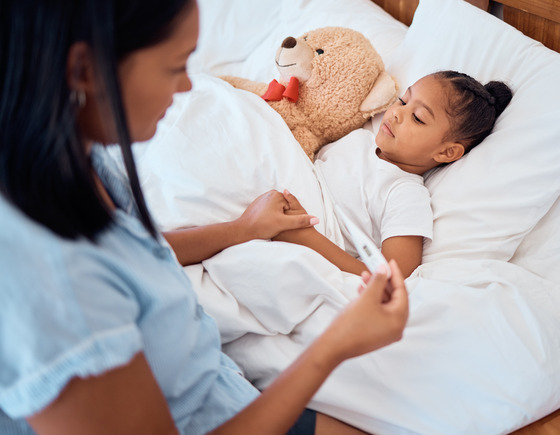Photo of a little girl in bed and her mom taking her temperature