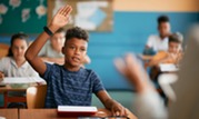 Photo of a boy in a classroom raising his hand