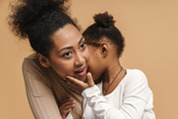 Photo of a little girl whispering in her mom's ear