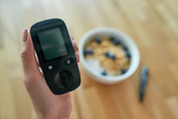 Photo of a person holding a blood glucose monitor with a healthy breakfast bowl