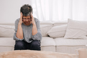 Photo of a woman sitting on a couch holding her hands to her head
