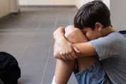 Photo of a sad little boy sitting on the floor in the hallway of a school