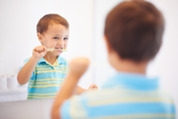 Photo of a little boy brushing his teeth and looking into the mirror