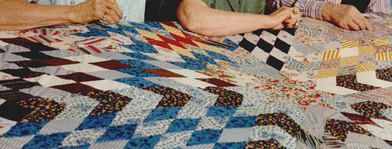 Women piece and sew a large quilt together, with the quilt pattern in the foreground