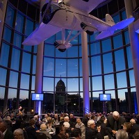 Devon Hall at night at the Oklahoma History Center with blue and violet lighting and the OK Capitol in the distance