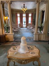 A Wedding Cake sitting on a table in front of chairs for wedding guests at the Overholser Mansion
