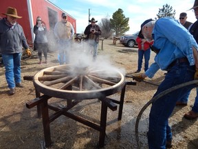 Blacksmith sets a ring in place onto a wooden wagon wheel