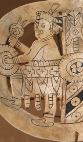 Spiro figures carved into a shell fragment, opposing each other in ceremonial dress