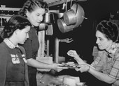 Aunt Susan, wearing an apron, demonstrates cooking to two women