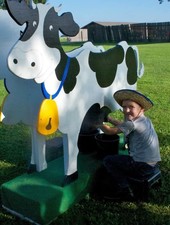 Child with a cowboy hat sits "milking" a wooden cow cut out