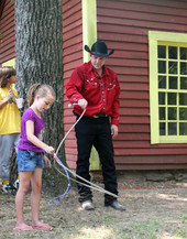 A man dressed in cowboy gear teaches youngsters how to make a lasso