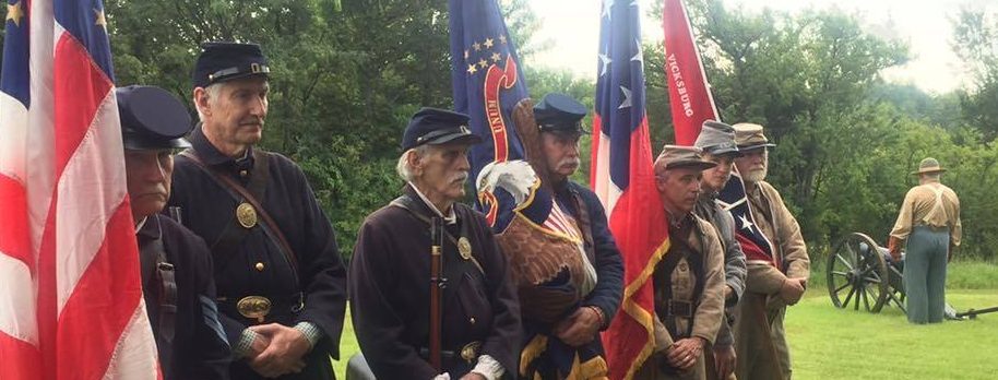 A group of reenactors in Civil War uniforms, holding state flags and US flag