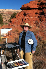 Artist Dallas Mayer stands by her painting easel in a canyon setting