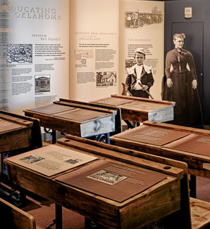 Education exhibit with school desks and a schoolmarm cut out at the Oklahoma History Center Sam Noble gallery
