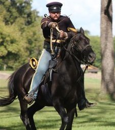 A living history reenactor charging on horseback in an 1848 uniform