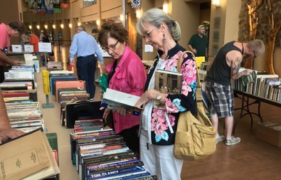 Research Center Book Sale with people at tables of books, opening, reading, and looking at the items on sale at the OHC