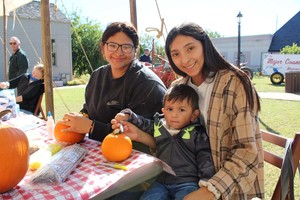 A Family seated together at a craft table with a red checkerboard cloth, painting a pumpkin