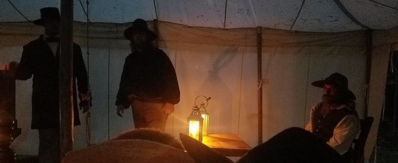 Reenactors standing in a tent with lanterns lit at night.