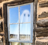 A Ghost figure stands inside a window of Pawnee Bill's original log home, a reflection of the acreage is also seen in the window