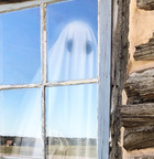 A Ghost figure stands inside a window of Pawnee Bill's original log home, a reflection of the acreage is also seen in the window