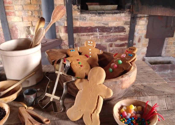 A wooden table with baked gingerbread men, some decorated, and the Fort Gibson bake ovens in the background