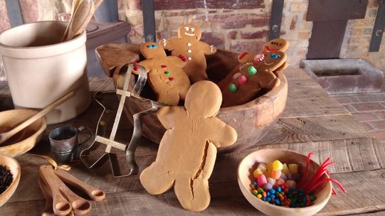 A wooden table with baked gingerbread men, some decorated, and the Fort Gibson bake ovens in the background