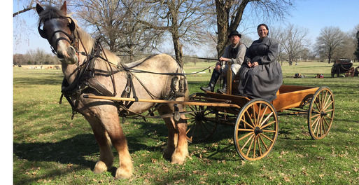 Living History reenactors and Ft. Towson site director in period clothing sitting on the buckboard of a horse-drawn wagon