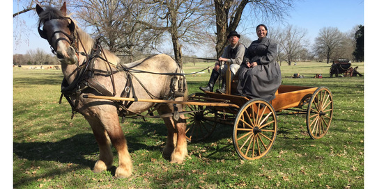 Living History reenactors and Ft. Towson site director in period clothing sitting on the buckboard of a horse-drawn wagon