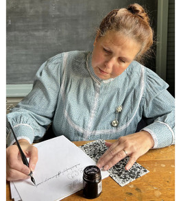 a living history reenactor dressed as a schoolteacher at the CSRHC writing with pen and ink at a schooldesk
