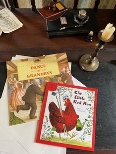 A photograph of children's books laying on an old-fashioned desk with a candle nearby