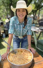 Maggie Harris standing with a cowboy hat on displaying a cobbler made at the Chuck Wagon gathering