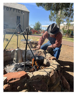 A living history reenactor stokes an outdoor fire by the US Land Office in Enid