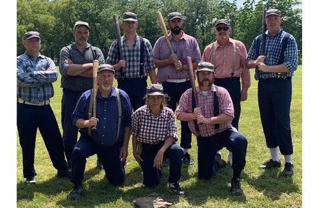 A group of Men and one woman dressed in 1800s baseball attire-- knickers, suspenders, and shirts, some holding baseball bats