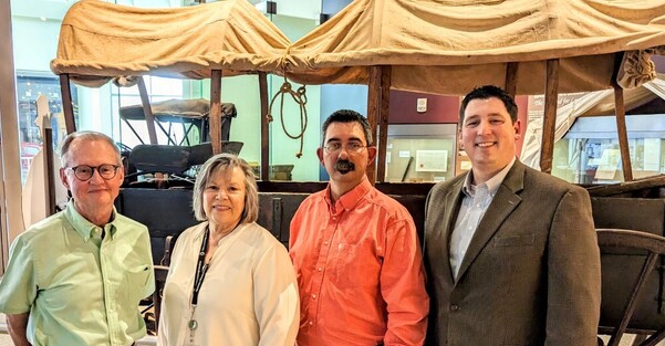 Dr. Bob Blackburn, Kathy Dickson, Jason Harris, and Trait Thompson standing in front of a covered wagon exhibit
