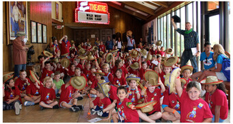 A group of Wild West Kids Camp campers wave their cowboy hats in the air