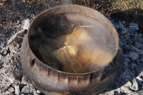A cast iron cooking vessels with tied corn husk bundles on a fire—traditional Choctaw foodways being demonstrated.